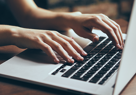 Close-up of hands typing on a laptop keyboard.